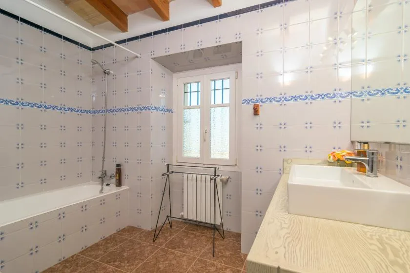 A tiled bathroom with a white sink and a window above the radiator.