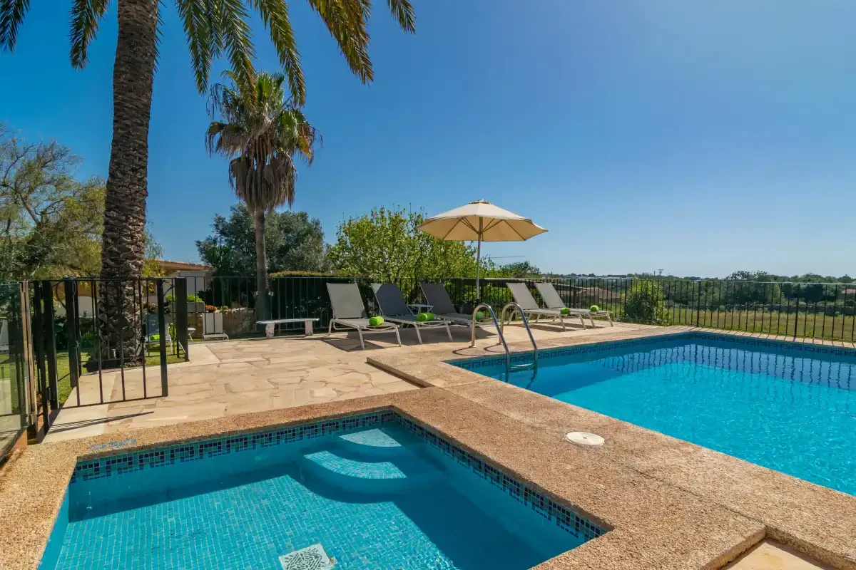 An outdoor swimming pool and spa sit beside a sunny patio with lounge seating.