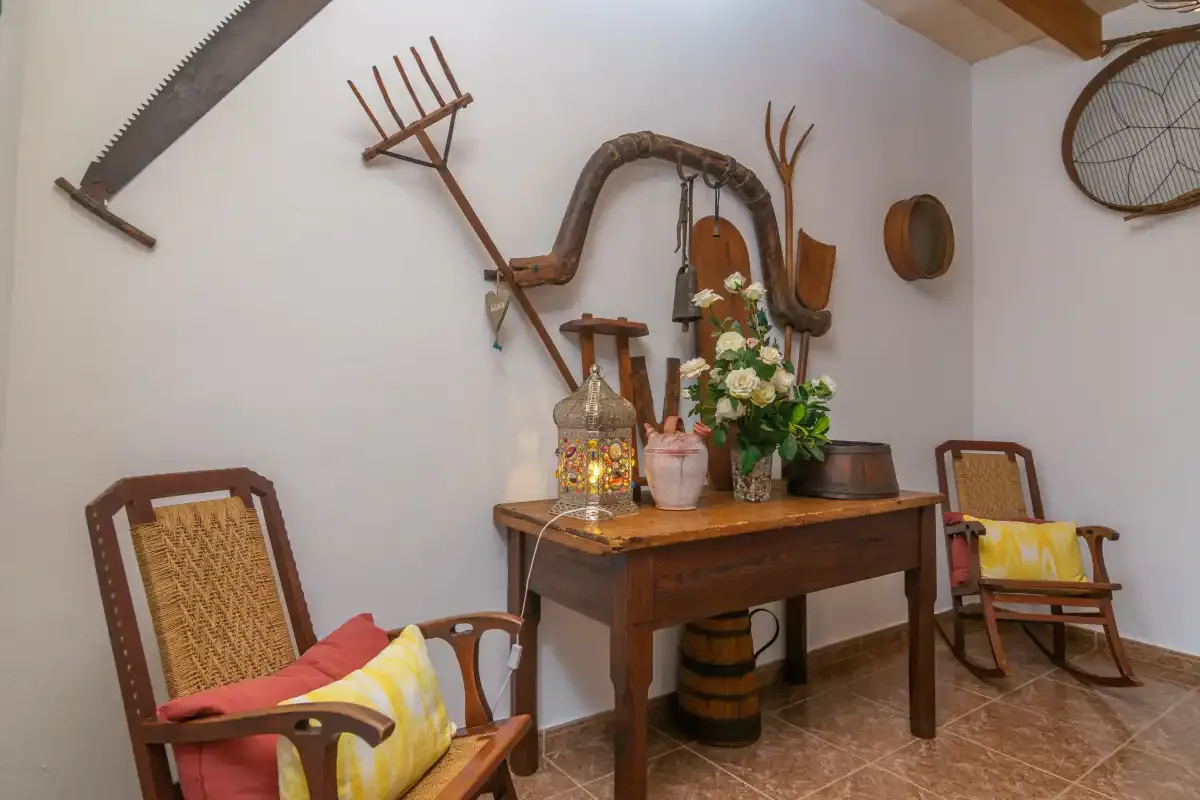 A rustic interior displays wooden furniture, flowers, and traditional tools on the walls.