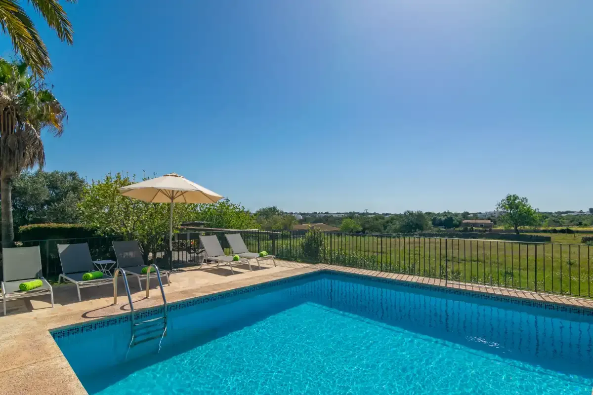 An outdoor swimming pool beside a patio with loungers and an umbrella.