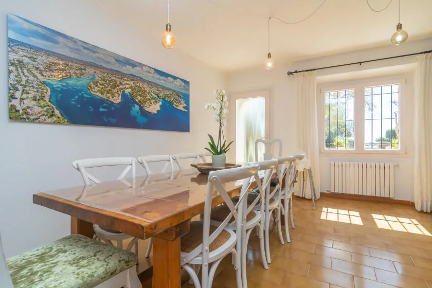 A bright dining room with a long wooden table and chairs beside sunny windows.