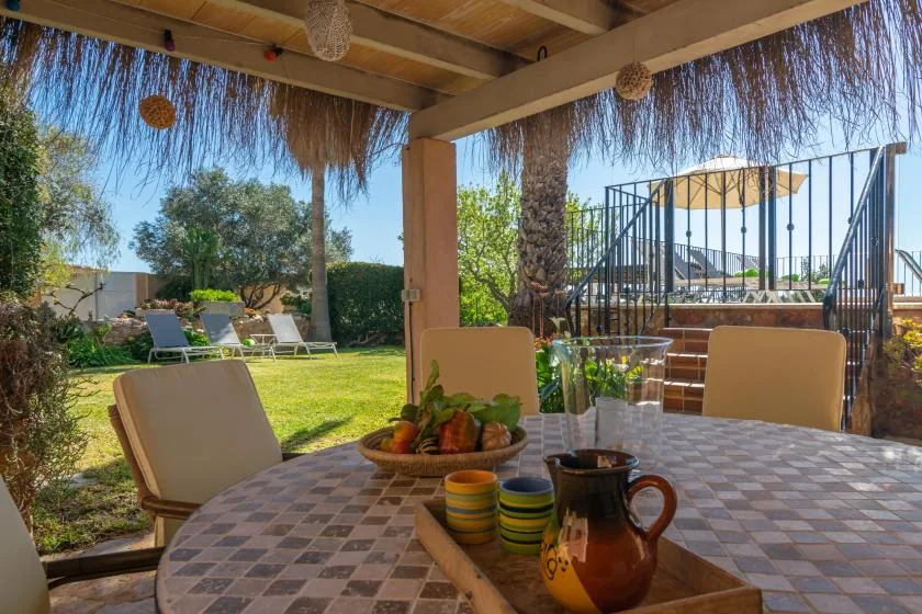 A covered outdoor dining area overlooks a lawn and garden seating.