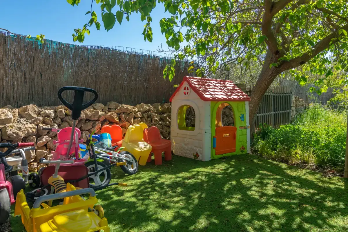 A children's play area in a garden with a small playhouse and ride-on toys.