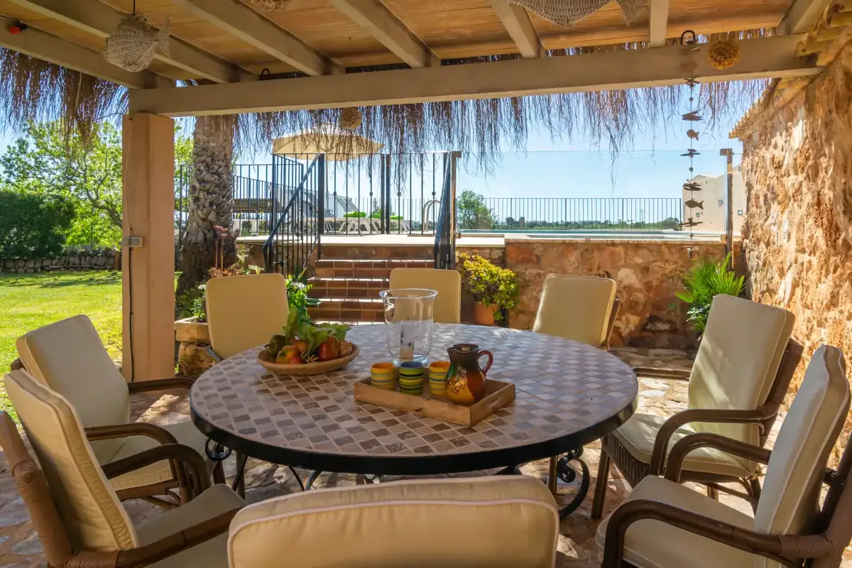 A covered outdoor dining area with a round table and surrounding seating.
