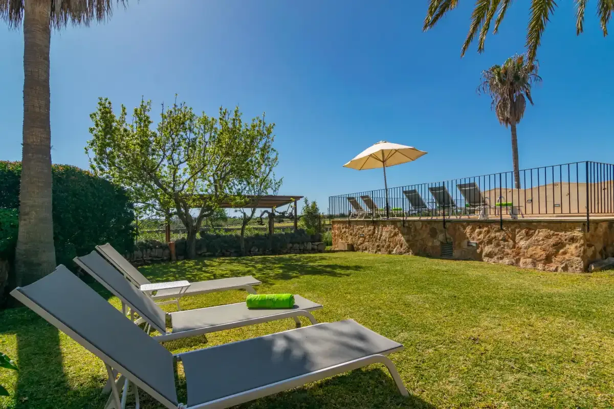 A sunny garden patio with reclining loungers, an umbrella, and a raised terrace.