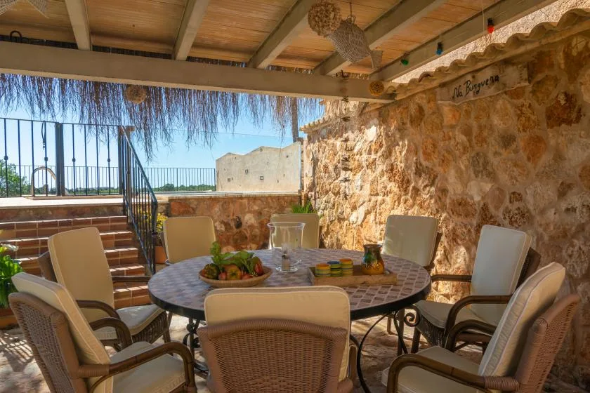 A shaded outdoor dining area with a round table and cushioned seating.