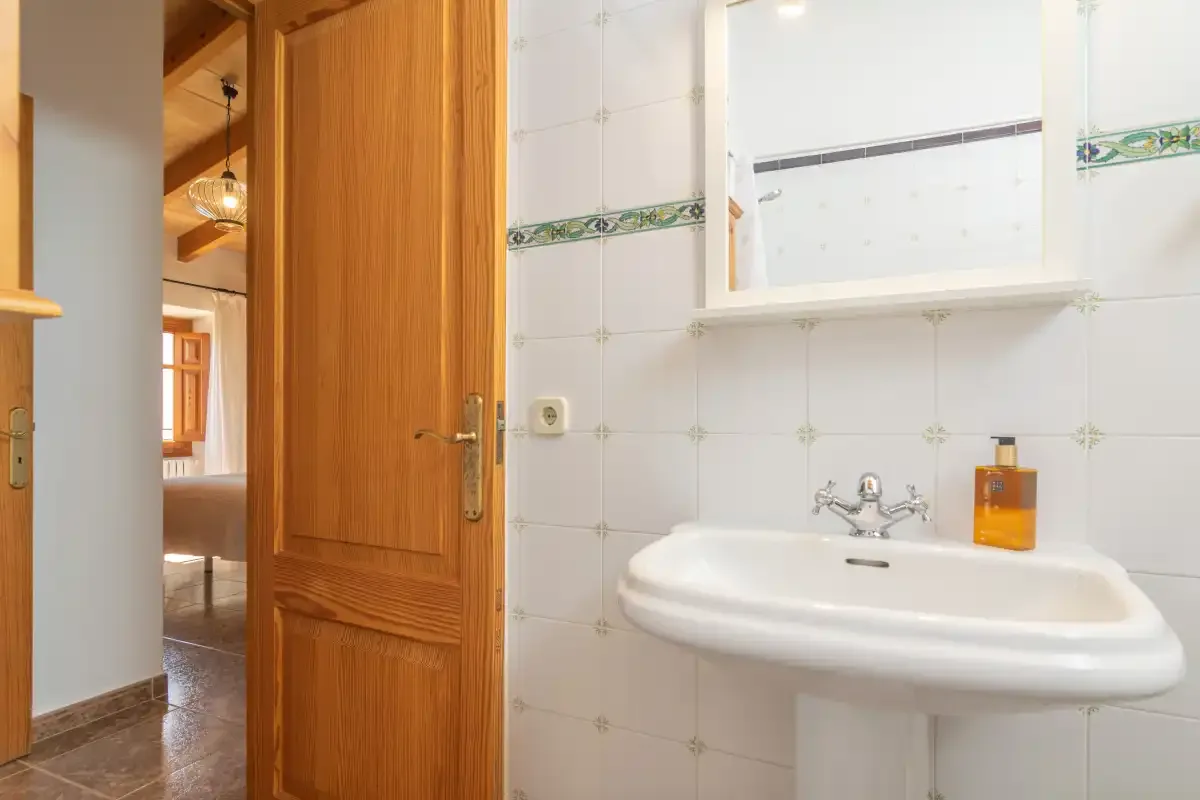 A tiled bathroom with a wall-mounted sink and an open wooden door.