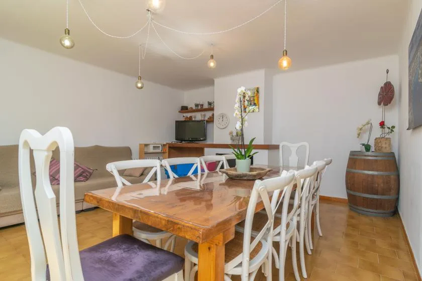 A dining area with a wooden table, white chairs, and a small television.