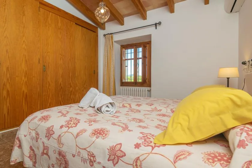 A bedroom with a floral bedspread, wooden wardrobe, and a window.