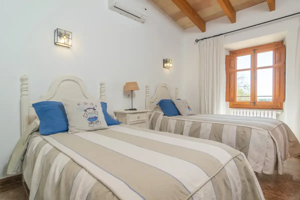 A twin bedroom with two beds, a wooden window, and exposed ceiling beams.