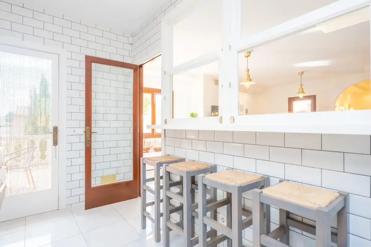 Una barra de cocina con azulejos claros tiene varios taburetes bajo una amplia abertura.