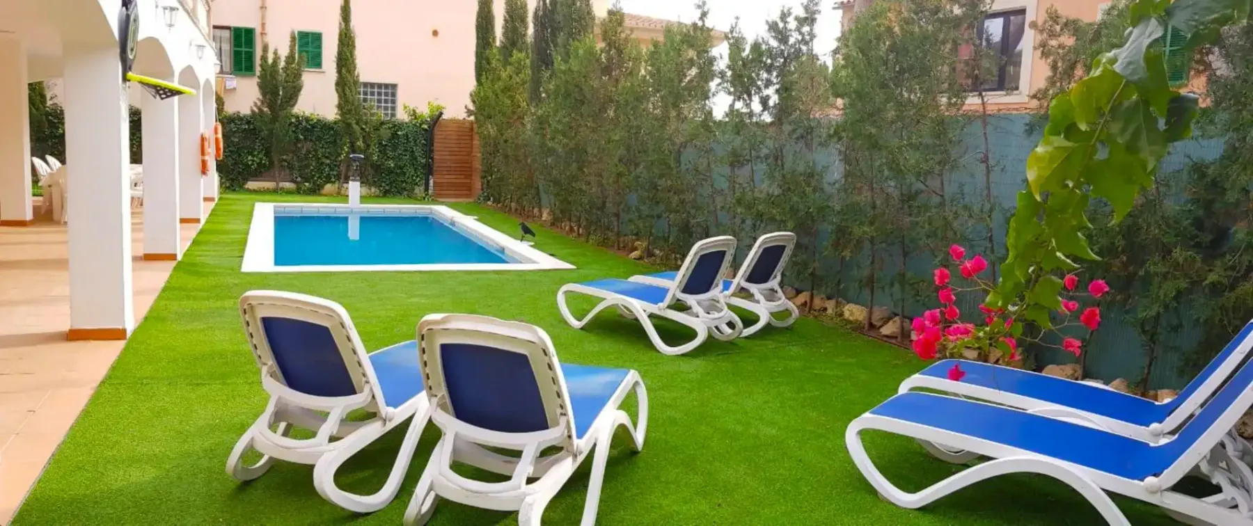Un jardín con una piscina rectangular y asientos reclinables.