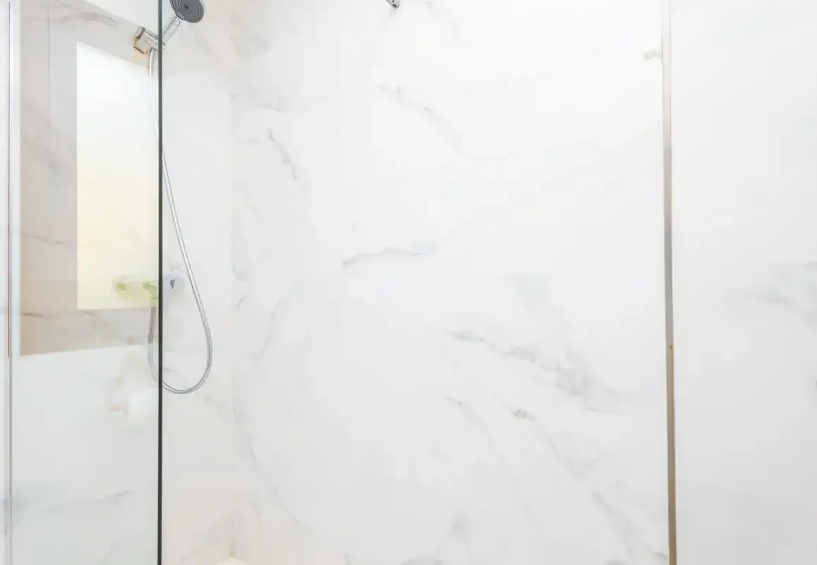 Una ducha de baño luminosa con paneles blancos veteados.