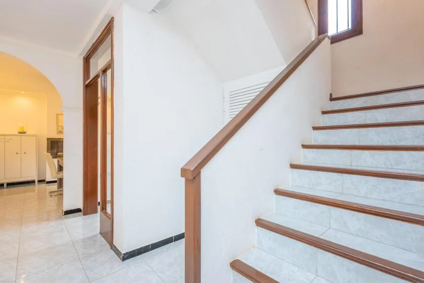 Una escalera de baldosas con pasamanos de madera sube junto a una puerta abierta.