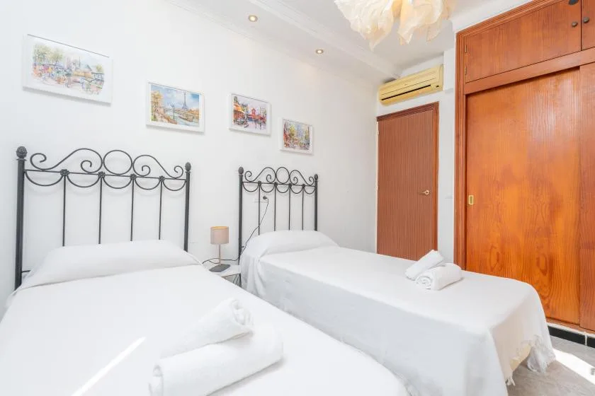 Un dormitorio con dos camas, ropa de cama blanca y cuadros en la pared.