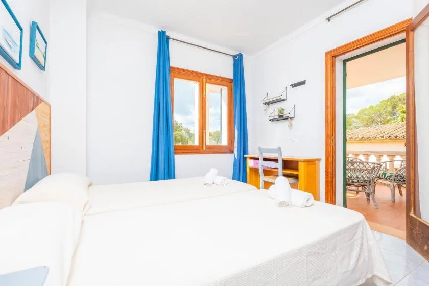 Un dormitorio luminoso con una cama blanca, cortinas azules y una puerta abierta al balcón.