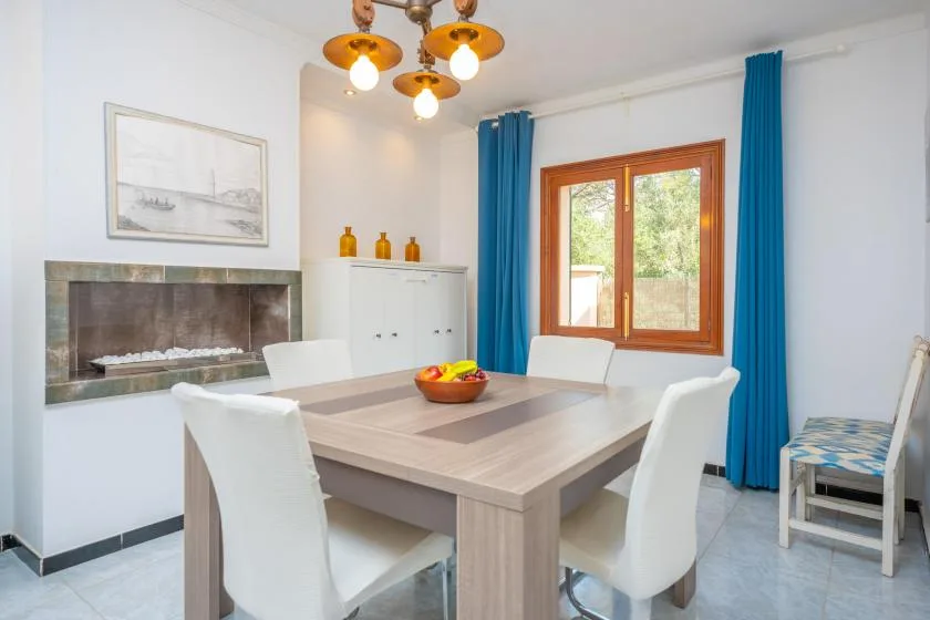 Un comedor luminoso con una mesa grande y una ventana enmarcada por cortinas azules.
