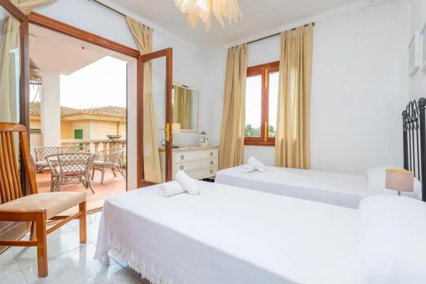 Un dormitorio luminoso con ropa de cama blanca y una puerta abierta a un balcón.