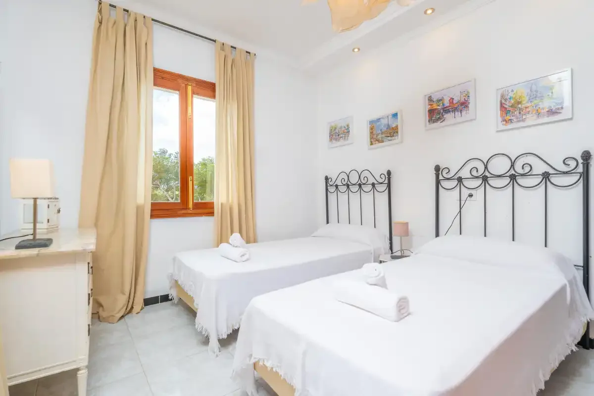 Un dormitorio luminoso con dos camas y una ventana enmarcada por cortinas beige.