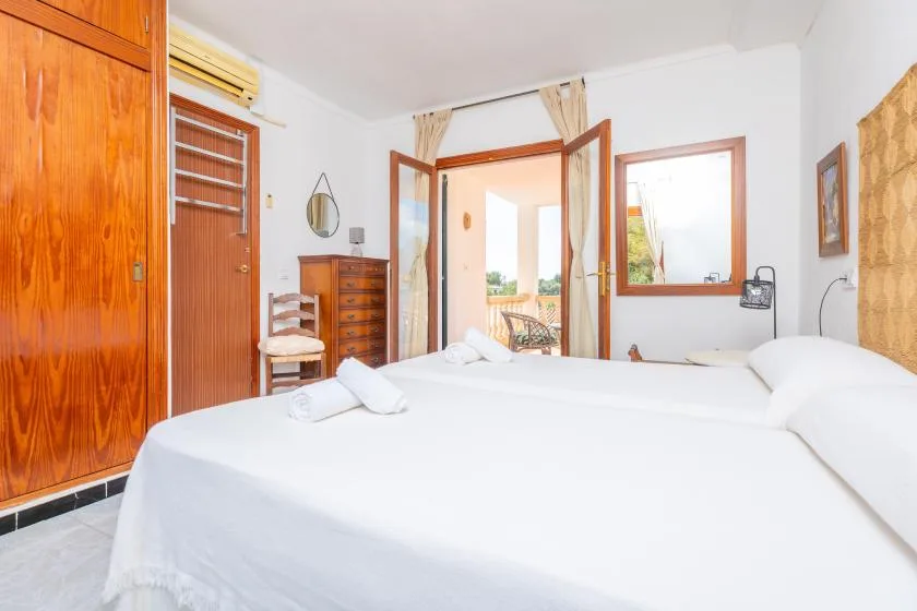 Un dormitorio luminoso con ropa de cama blanca y puertas de madera abiertas.