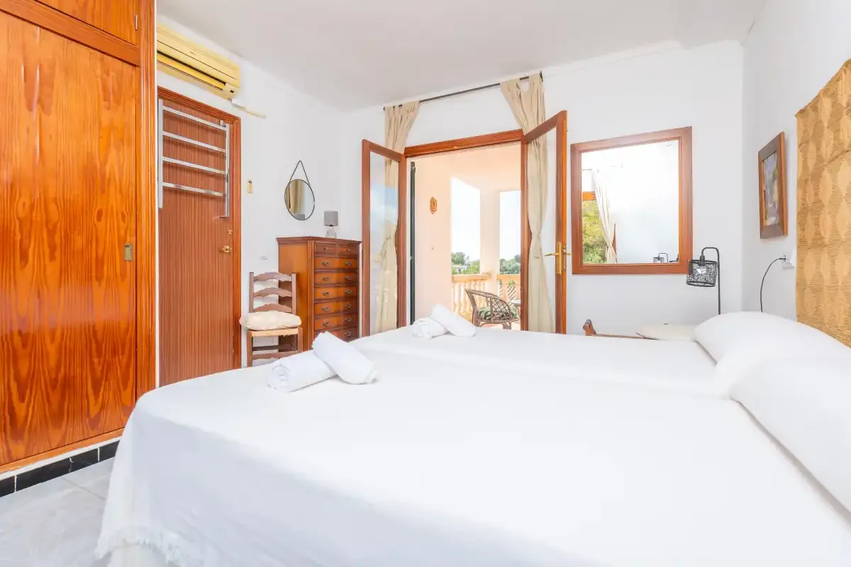 Un dormitorio luminoso con ropa de cama blanca y una puerta abierta a un balcón.