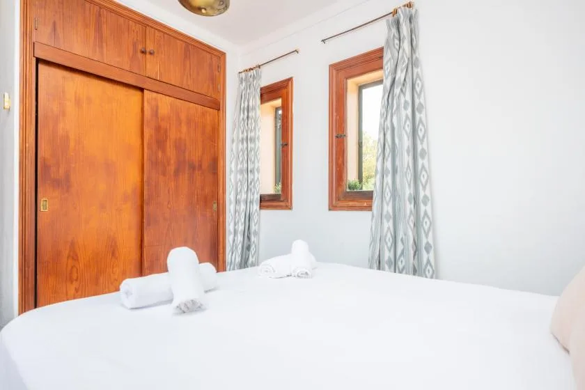 Dormitorio con una cama bien tendida, toallas y un armario de madera.