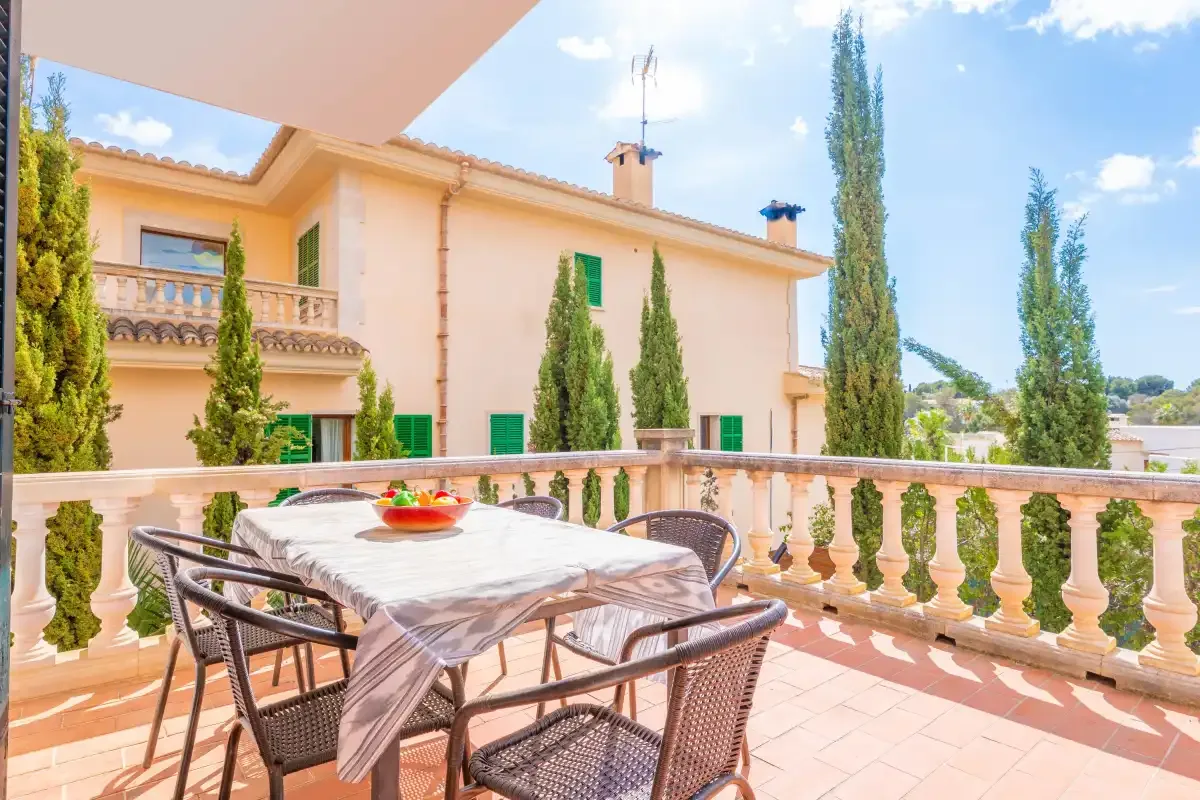 Una terraza soleada tiene una mesa de comedor exterior con vistas a un edificio color durazno.