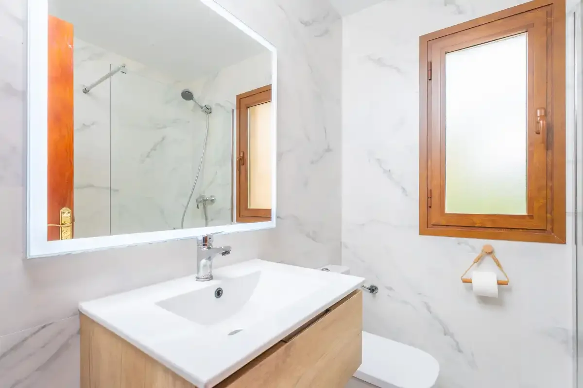 Un baño luminoso con lavabo, espejo y ventana con marco de madera.