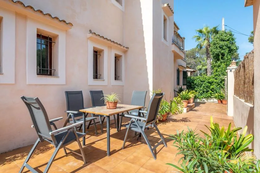 Un patio soleado con una mesa de comedor, asientos y plantas en macetas.