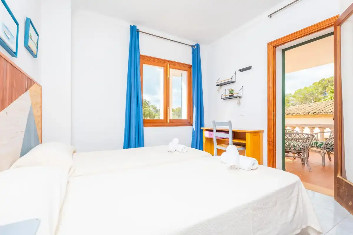 Un dormitorio luminoso con una cama blanca, cortinas azules y una puerta abierta.