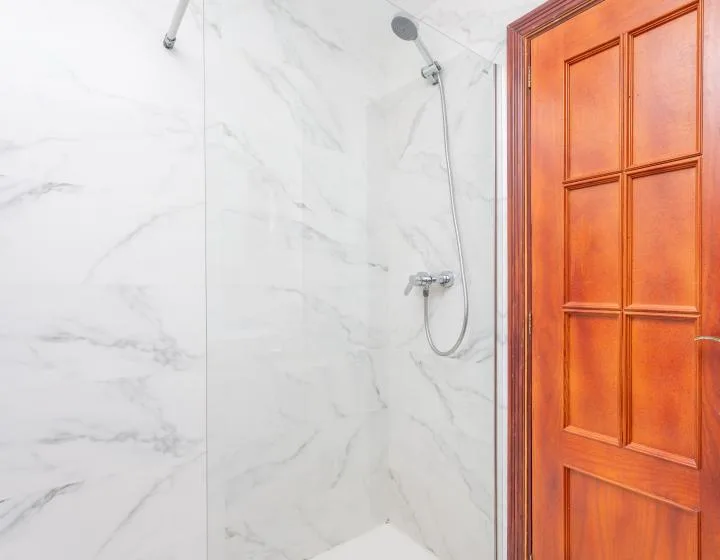 Una zona de ducha con acabado de mármol junto a una puerta de madera.
