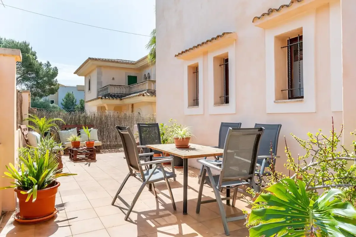Un patio soleado con una mesa, sillas y plantas en macetas.