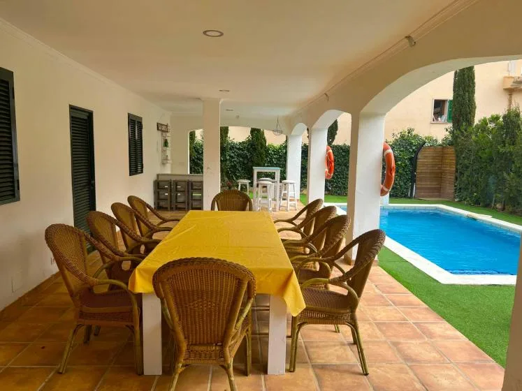 Una zona de comedor exterior cubierta con una mesa larga junto a una piscina.