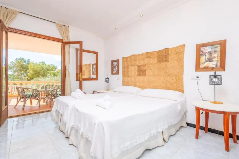 Un dormitorio luminoso con ropa de cama blanca y puertas abiertas hacia un balcón.