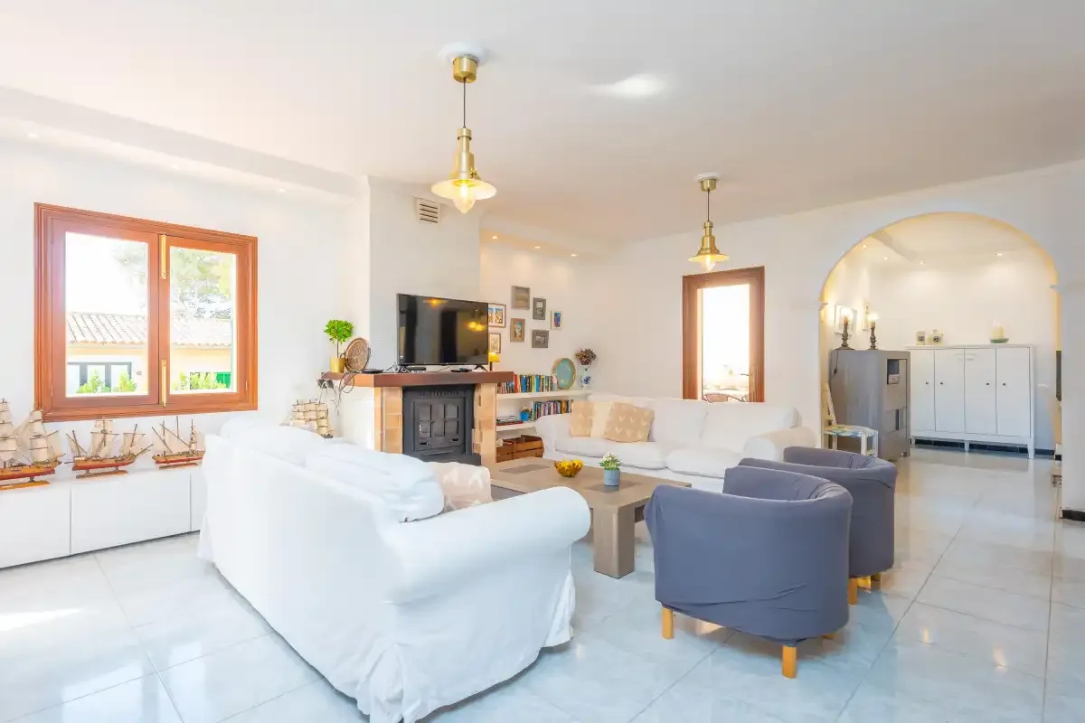 Un salón luminoso con asientos blancos, sillones azules y un televisor.