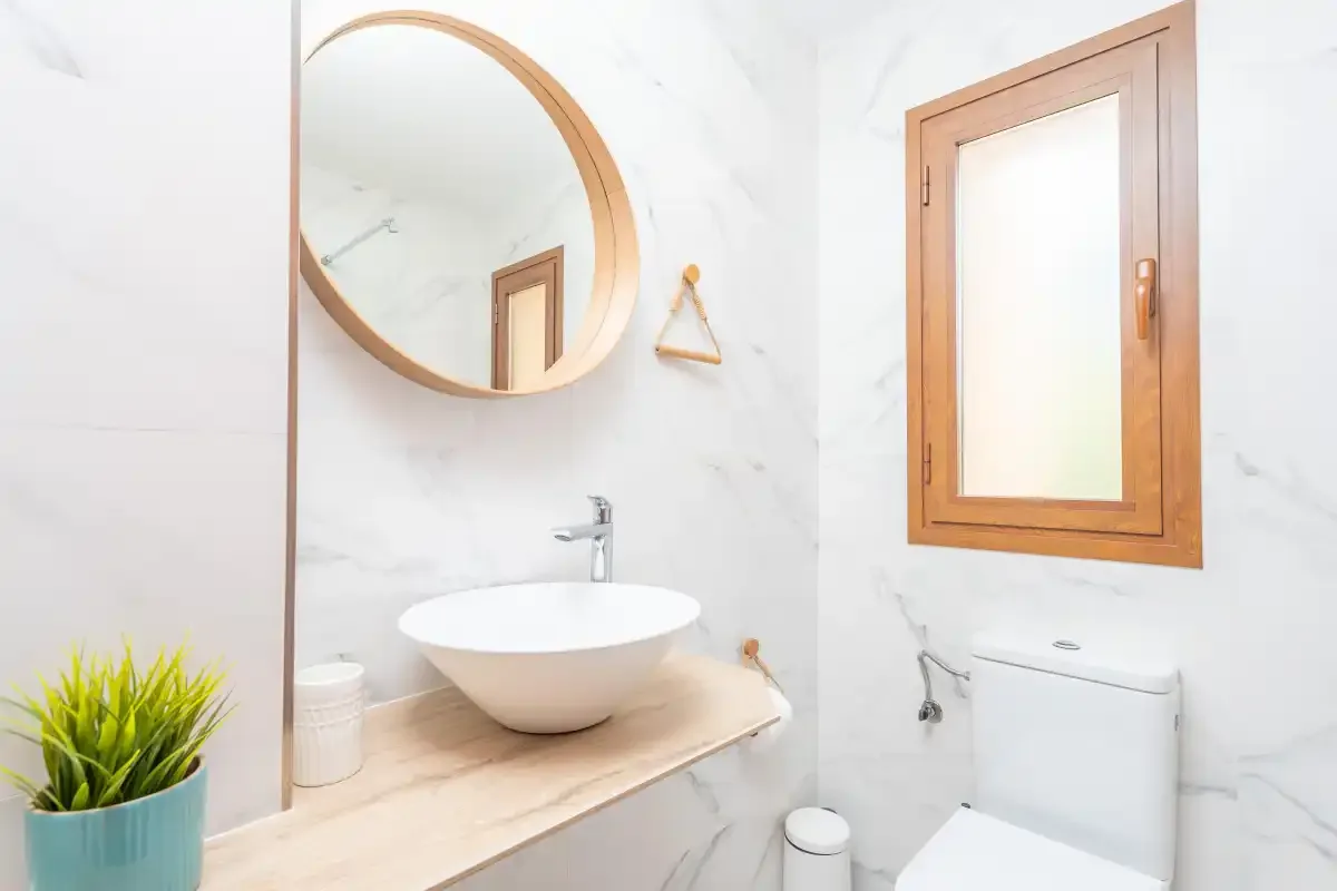 Un baño luminoso con lavabo sobre encimera, espejo redondo y ventana.