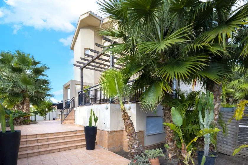 A multi-level building stands beside a tiled outdoor patio surrounded by palm trees.