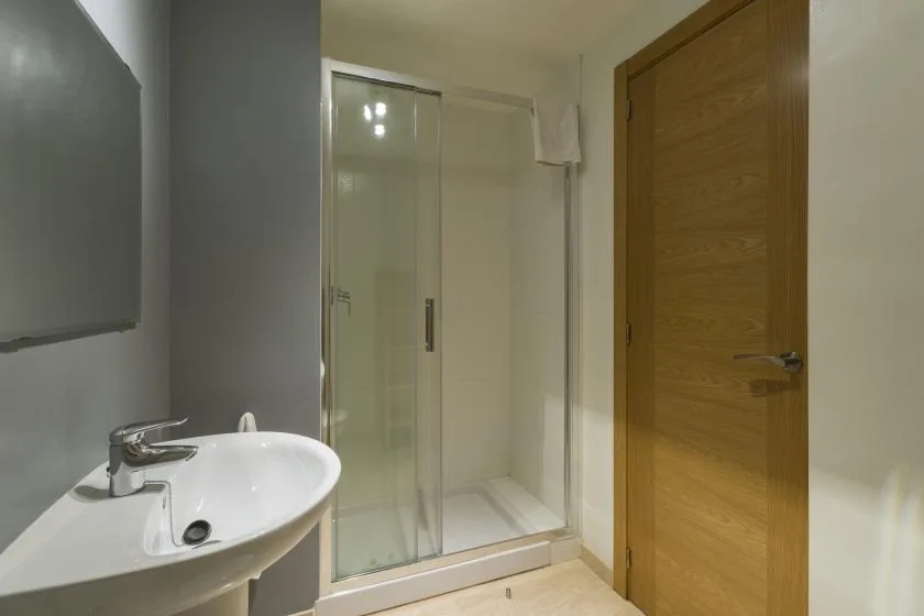 A bathroom with a glass shower, sink, and wooden door.