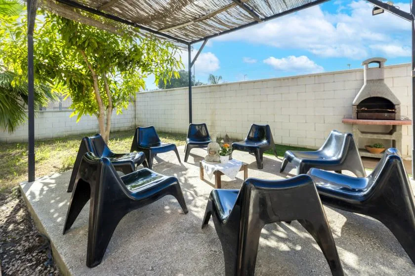 An outdoor seating area sits beneath a shaded pergola beside a built-in grill.