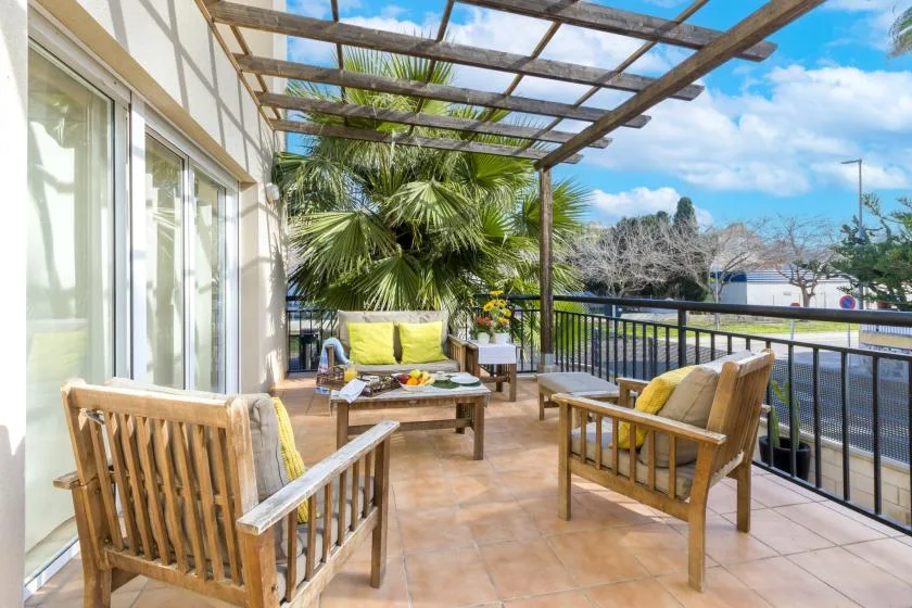 A tiled outdoor terrace with wooden seating beneath a pergola.