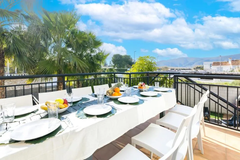 Outdoor dining area with a table set for a meal beside black railings and palm trees.