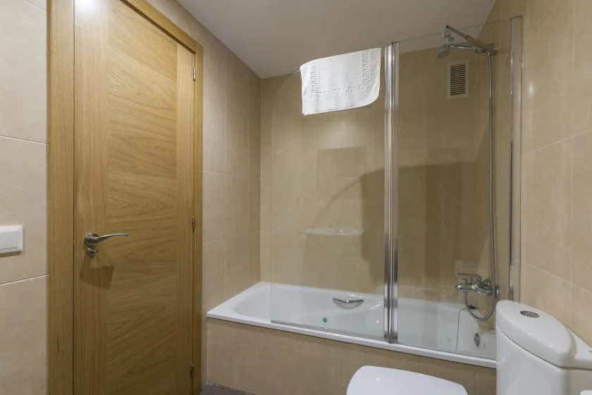 A tiled bathroom with a bathtub, glass shower screen, and wooden door.