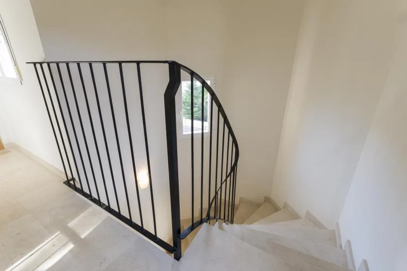 A curved staircase descends beside a black metal railing and a window.