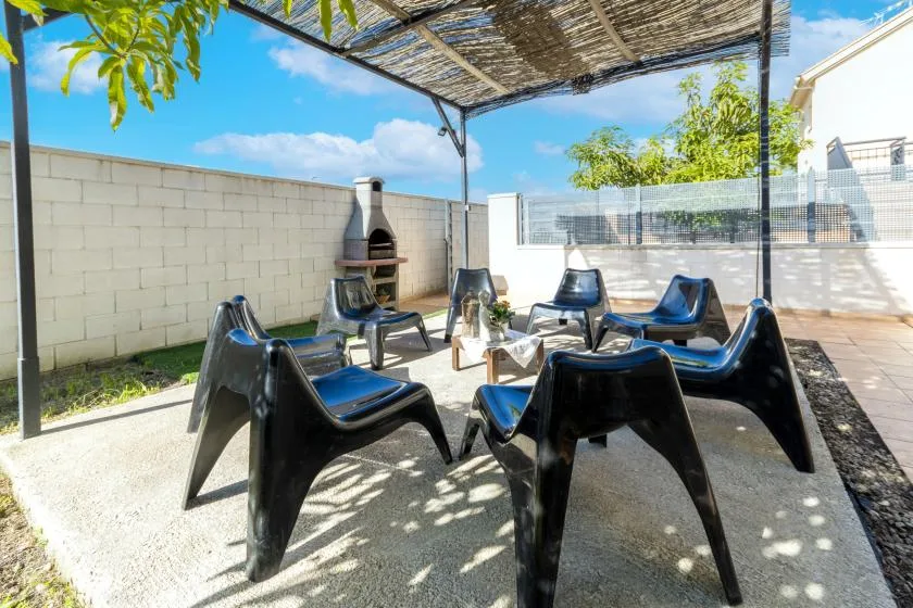 An outdoor seating area beneath a shaded canopy, with a brick barbecue nearby.