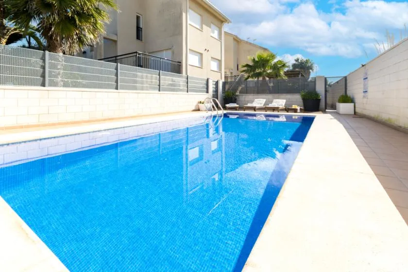 A bright outdoor swimming pool sits beside a paved patio and residential buildings.