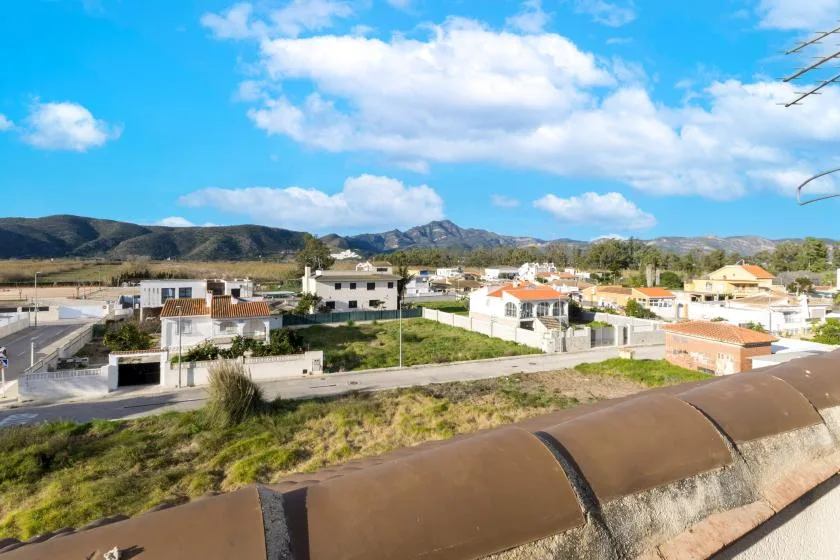 A view over a residential neighborhood toward distant hills beneath a cloudy sky.