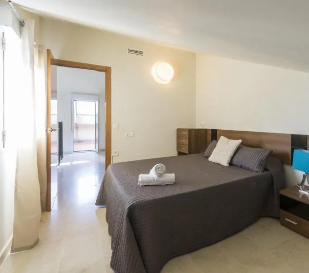 A bedroom with a neatly made bed and an open doorway to a bright adjoining space.