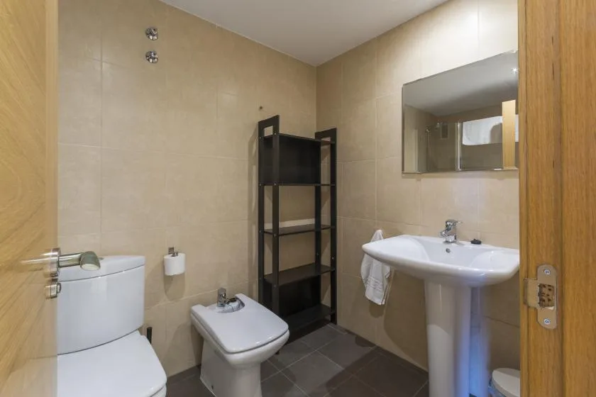 A tiled bathroom with a sink, toilet, and dark open shelving.