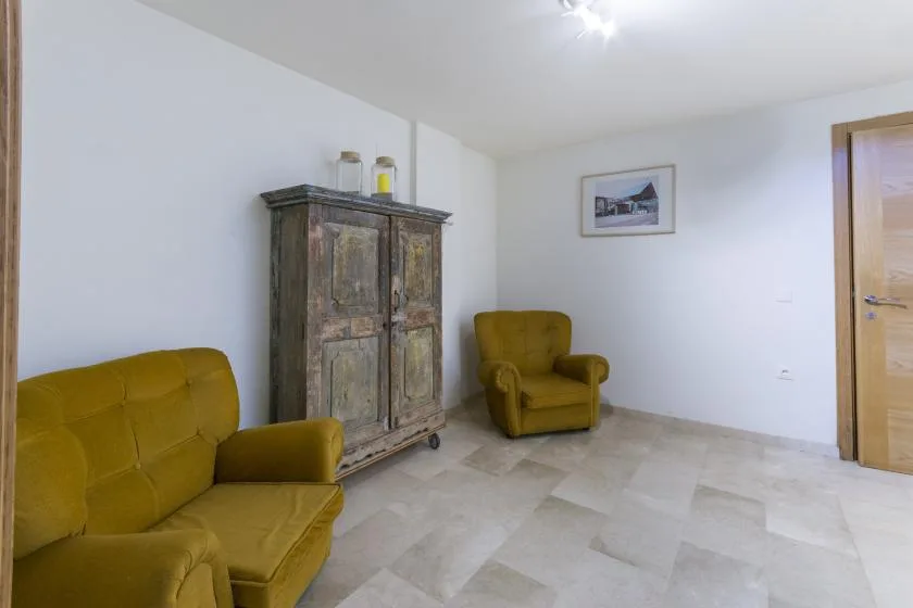 A living room with mustard-colored seating and a tall wooden cabinet.