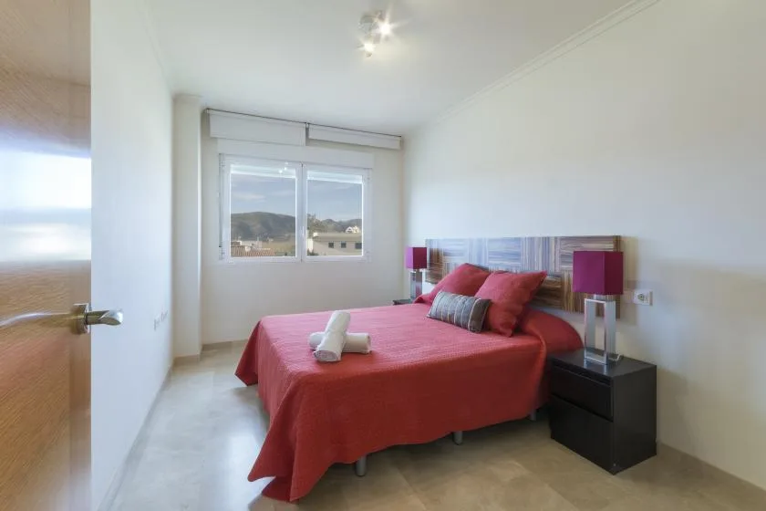 A bedroom with red bedding, bedside tables, and a window overlooking the outdoors.